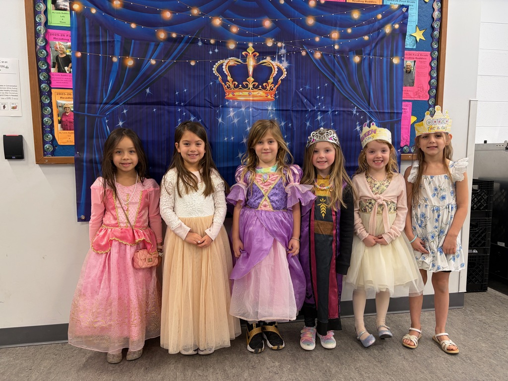 A line of smiling girls dressed like queens in front of a crown backdrop