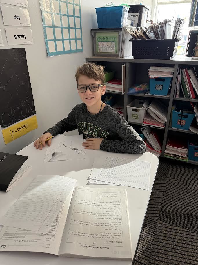 Fifth grade boy working on his ELA project at desk with papers spread out in front of him.