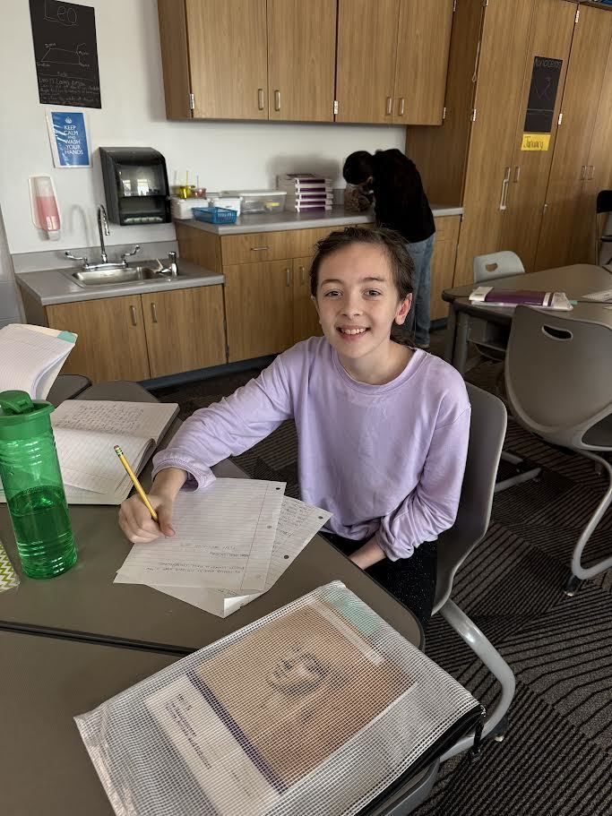 Fifth grade girl smiling at her desk working on her ELA project. 