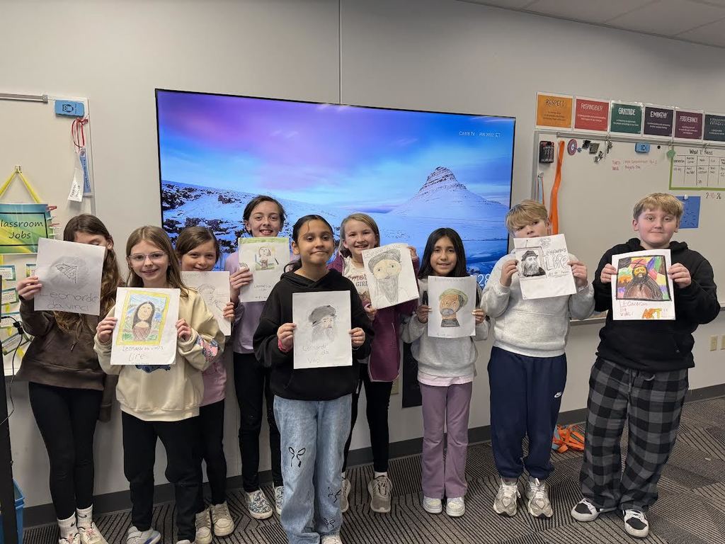A group of fifth grade students posing with their ELA projects at the front of the class.