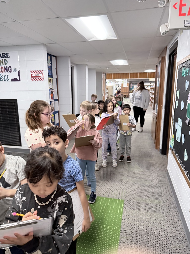 A line of first graders walking though the school hallways looking for light sources and taking notes.