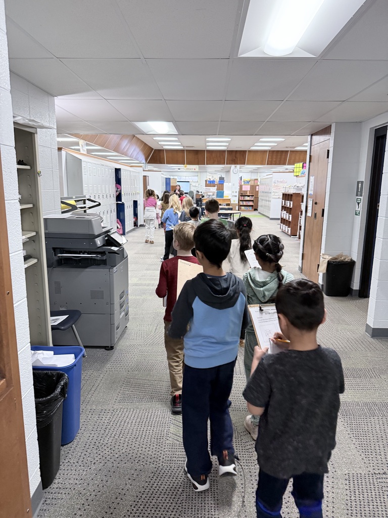 A line of 1st grade students from the back walking in the hallways taking notes on light sources.