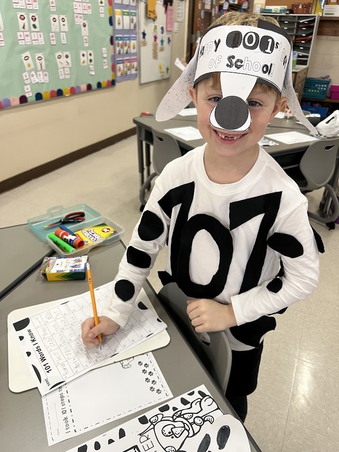Smiling first grade boy with Dalmatian spirit wear working on 101 days of school celebration assignment.