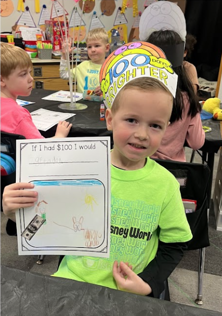 5K boy in a 100th day of school crown holding a finished celebration assignment.