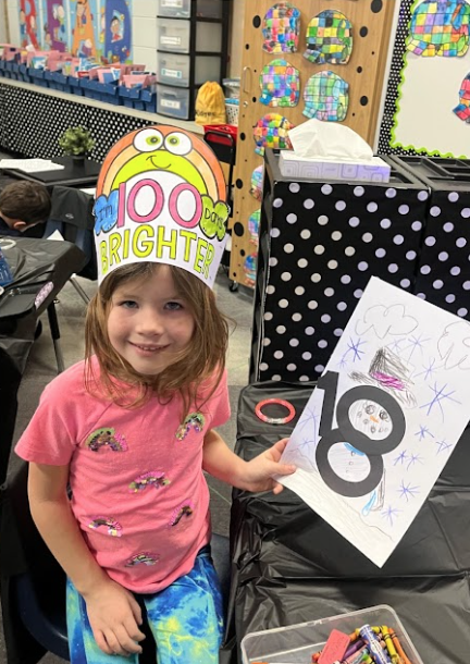 Smiling 5K girl in a 100th day of school crown showing off her celebration artwork creation.