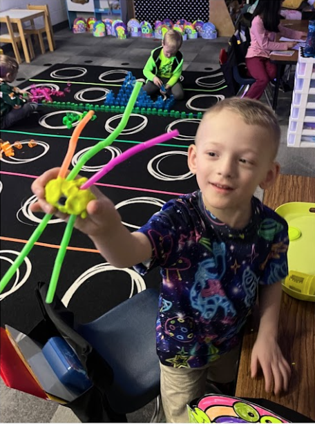 5K boy holding neon pipe cleaner creation, an activity celebrating the 100th day of school.