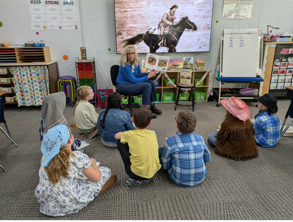 Students sitting on the floor listening to a volunteer read about Western Expansion.