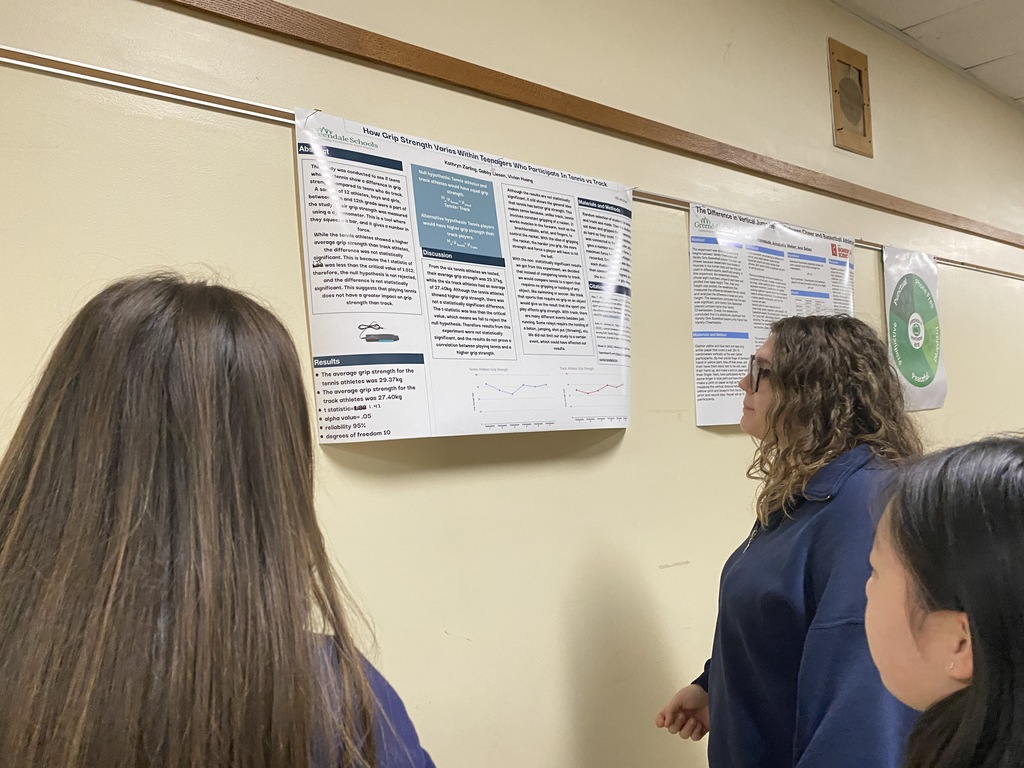Three individuals examining posters of academic presentations in a hallway.