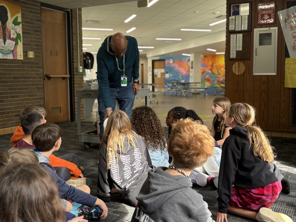 A man showing something to a group of children seated on a school hallway floor
