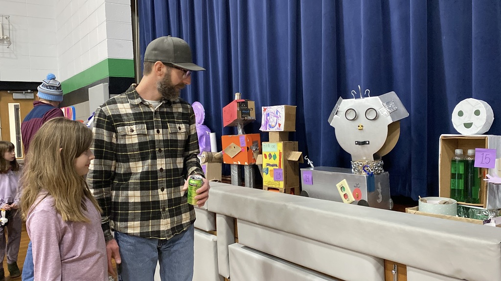 A man and a child observe cardboard robot models at an exhibition.