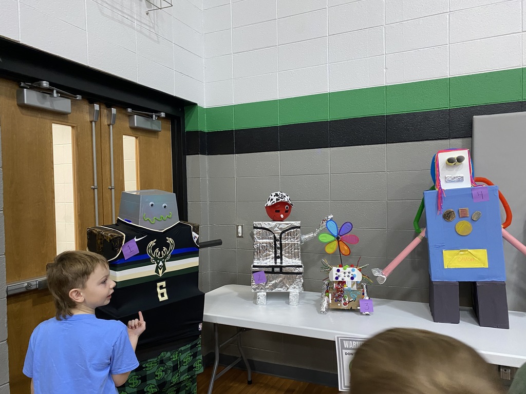 Three colorful and creative robot figures displayed on a table, with a child observing them.