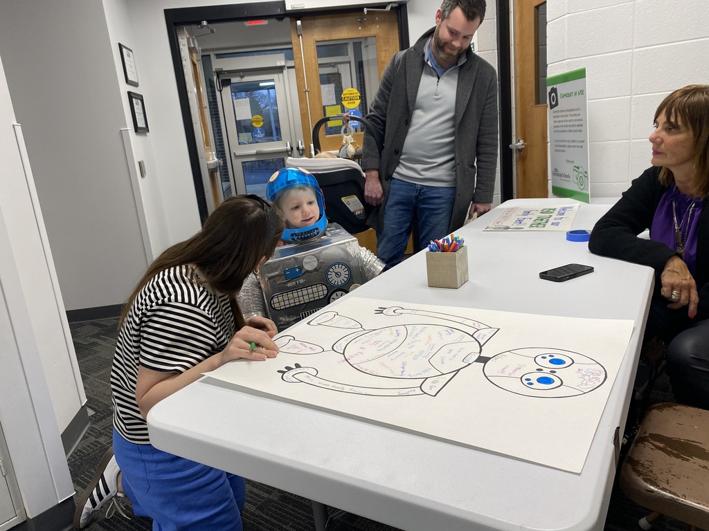 Child in a robot costume speaking to a woman who is kneeling beside him and writing  on a page.