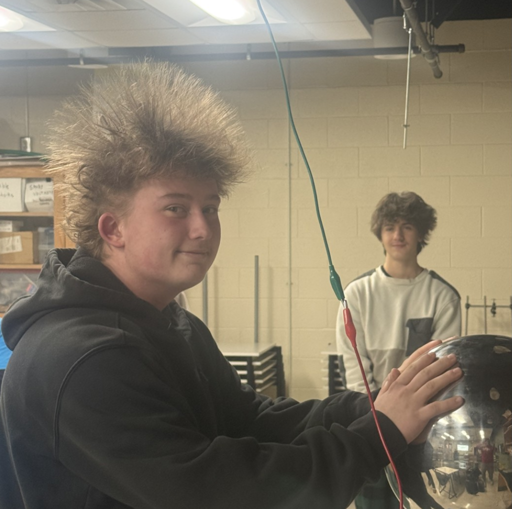 Student in Physics Class with hands on a generator and hair sticking up.