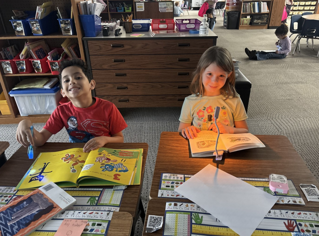 Two smiling students reading by flashlight during a Read Across America week activity.