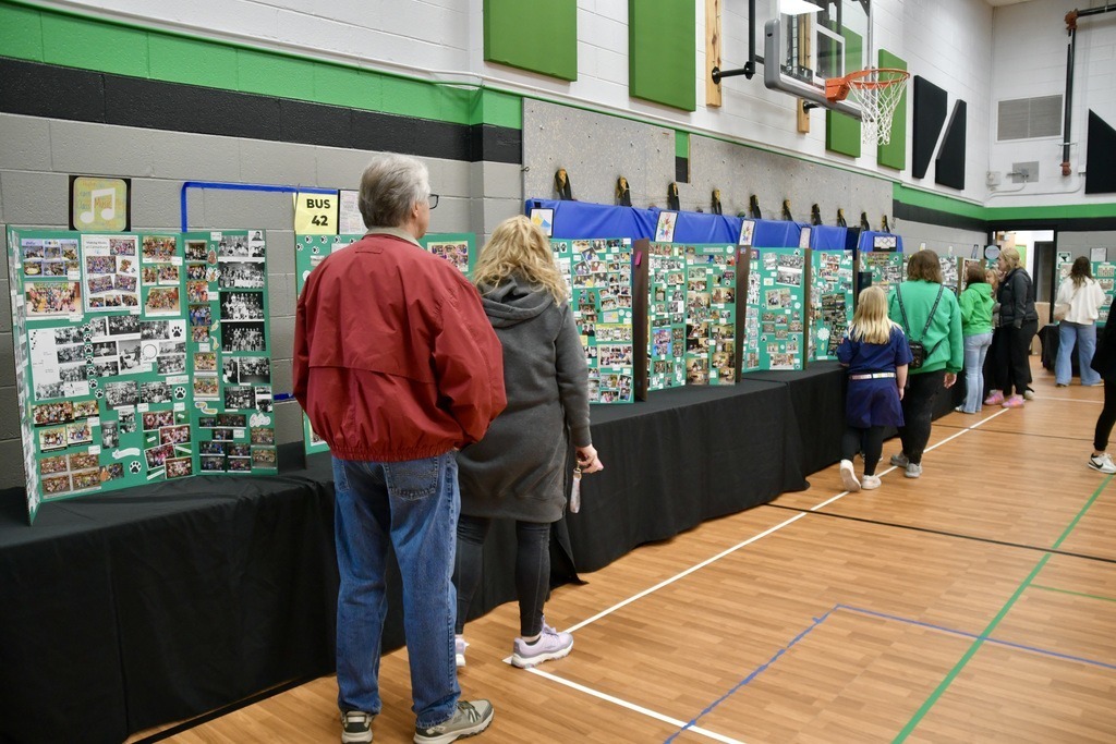 People viewing green display boards in a gymnasium.