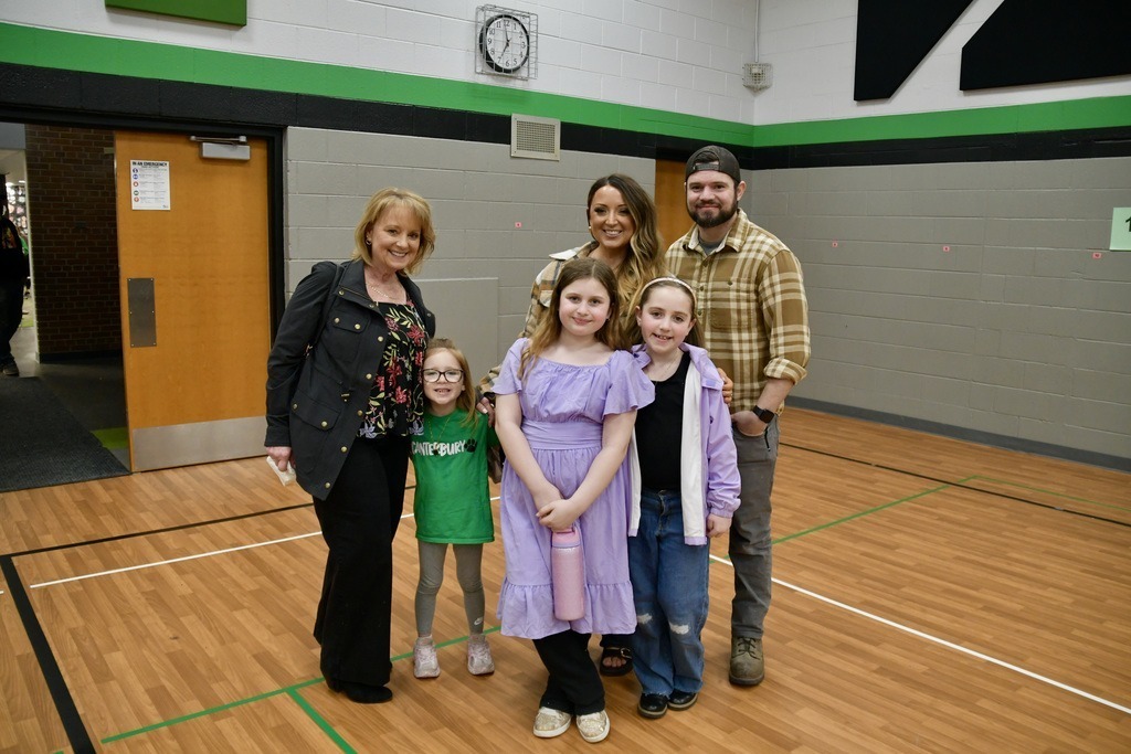A group of six people standing on a gym floor with gray and green walls.
