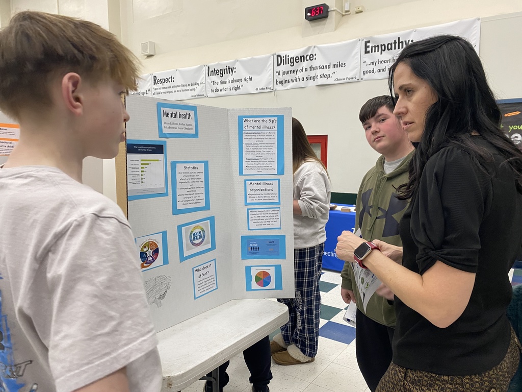 People listening to an 8th grader discuss his presentation board at the Wellness Fair.