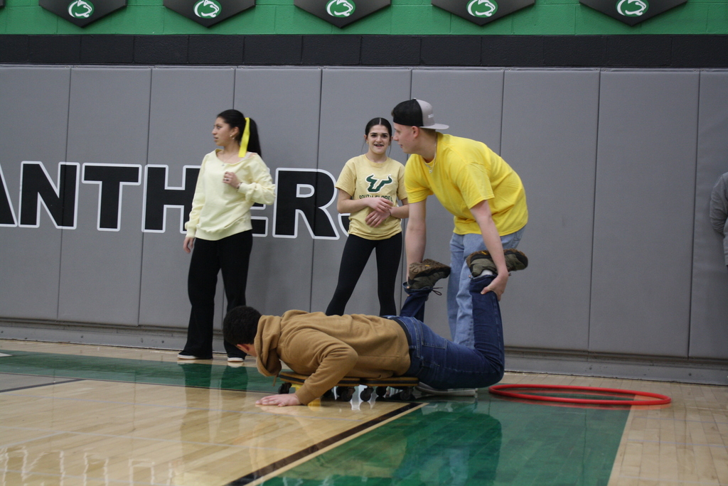 People participating in a team activity in a gym, with a person on a wheeled platform being assisted by another.