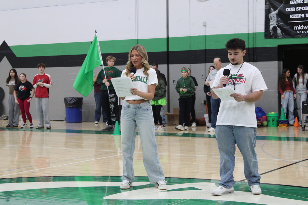 Two individuals holding microphones and papers in a gymnasium.