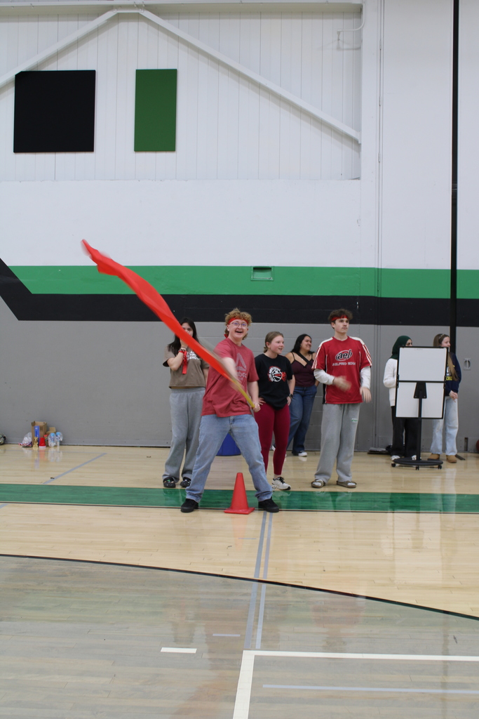 Group of young people in a gymnasium, one waving a red flag energetically.