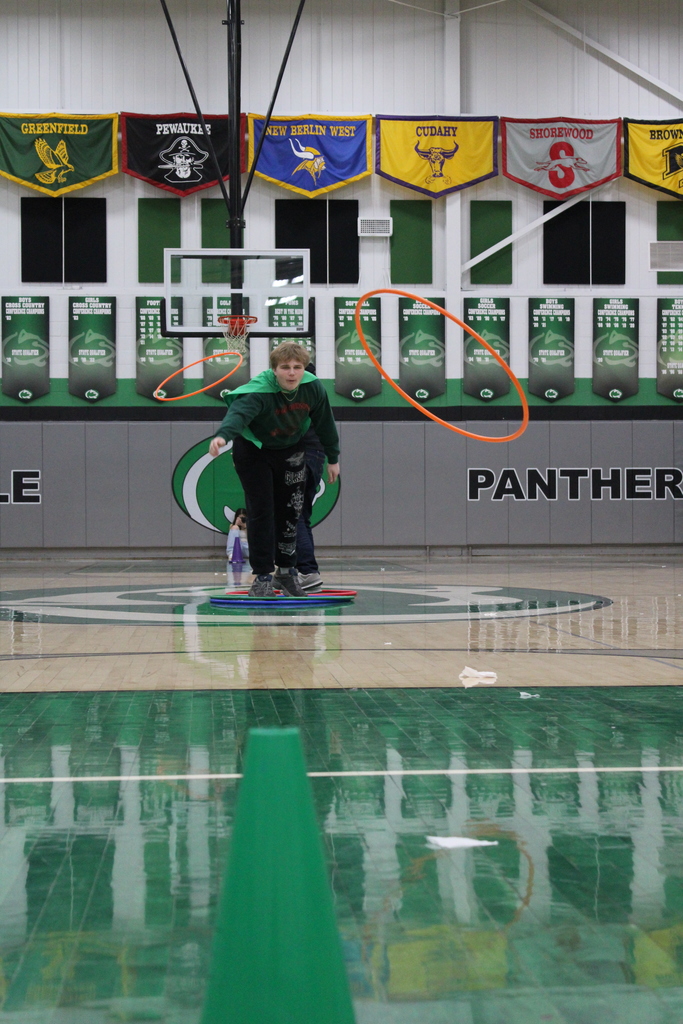 Person in a gymnasium stepping on a colorful mat with hula hoops suspended in the air around them.
