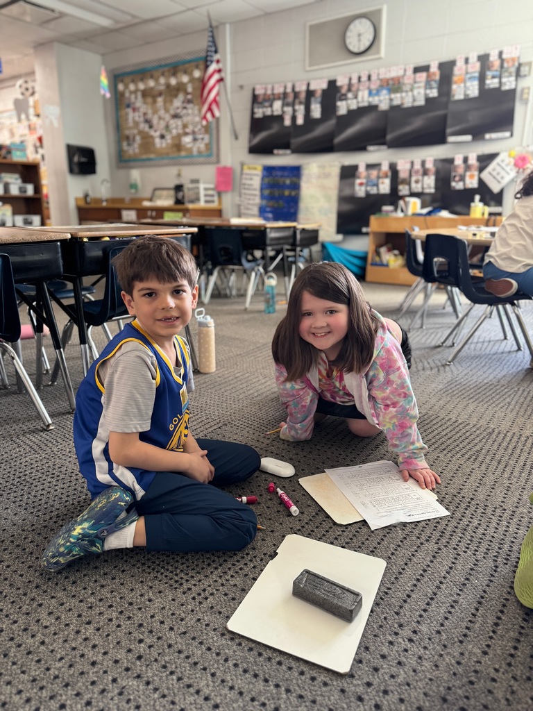 Two children sitting on the floor doing a math worksheet holding pencils.