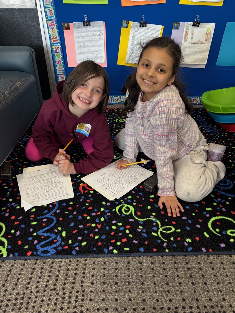 Two children sitting on the floor doing a math worksheet holding pencils.