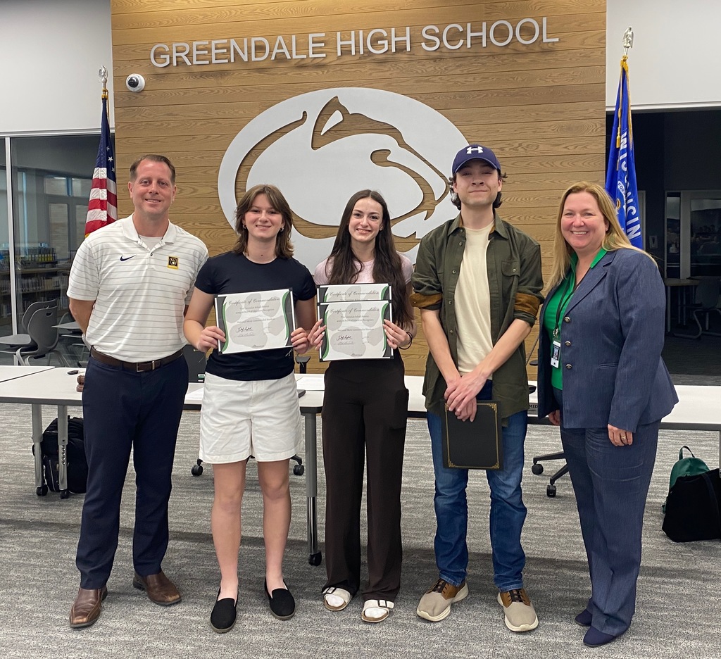 Five people standing in front of a "Greendale High School" sign, with two holding certificates.