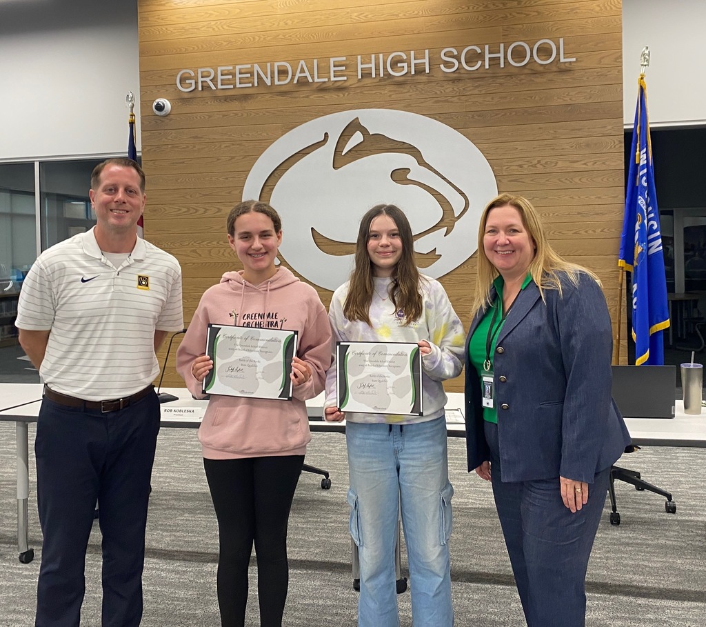 Four people stand in front of a "Greendale High School" sign, with two holding certificates.