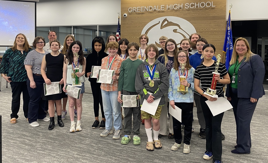 A group of students and adults pose with certificates and trophies in front of a wall with "Greendale High School" text and logo.