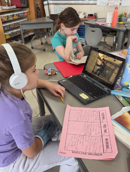 Astronomy: Two third grade students doing research by reading and working on the computer.