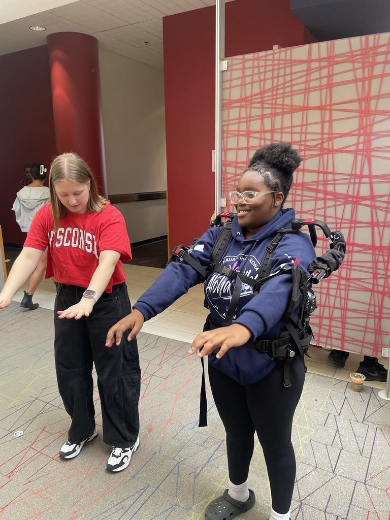 Student wearing a robotics device standing with an adult demonstrating it.