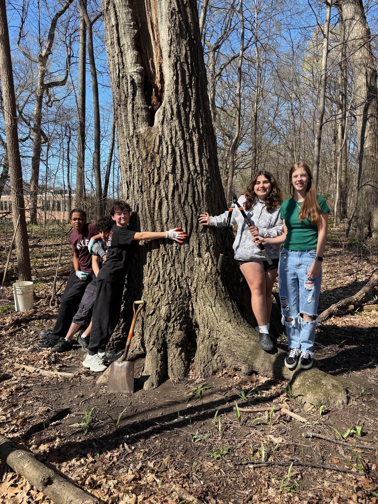 Several 8th graders posing with chopping tools as they cut buckthorn from the school woods in honor of Earth Day.