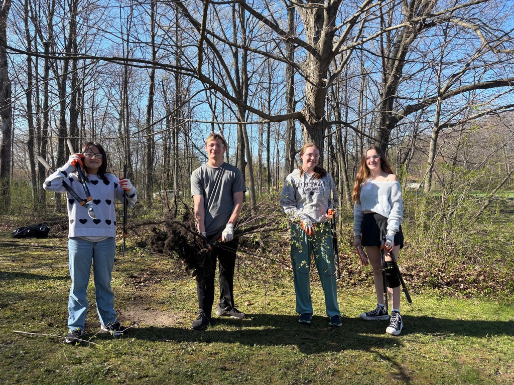 Several 8th graders posing with chopping tools as they cut buckthorn from the school woods in honor of Earth Day.