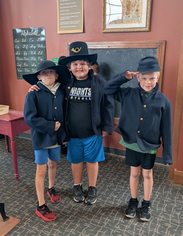 Three smiling boys dressed in Civil War Uniforms during a field trip.