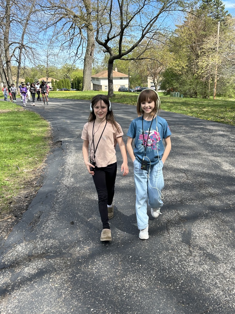 Two girls walking on a sidewalk with headphones during a Walking Classroom experience,