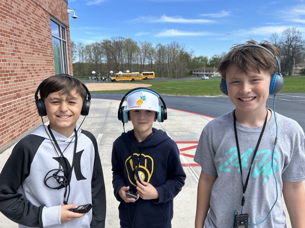 Three smiling boys with portable headphones posing while on a Walking Classroom experience.