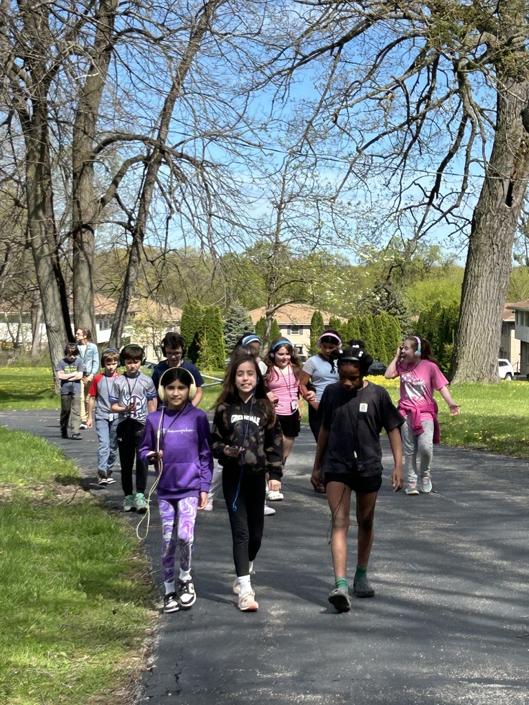 A group of students with headphones walking on a sidewalk during a Walking Classroom experience.