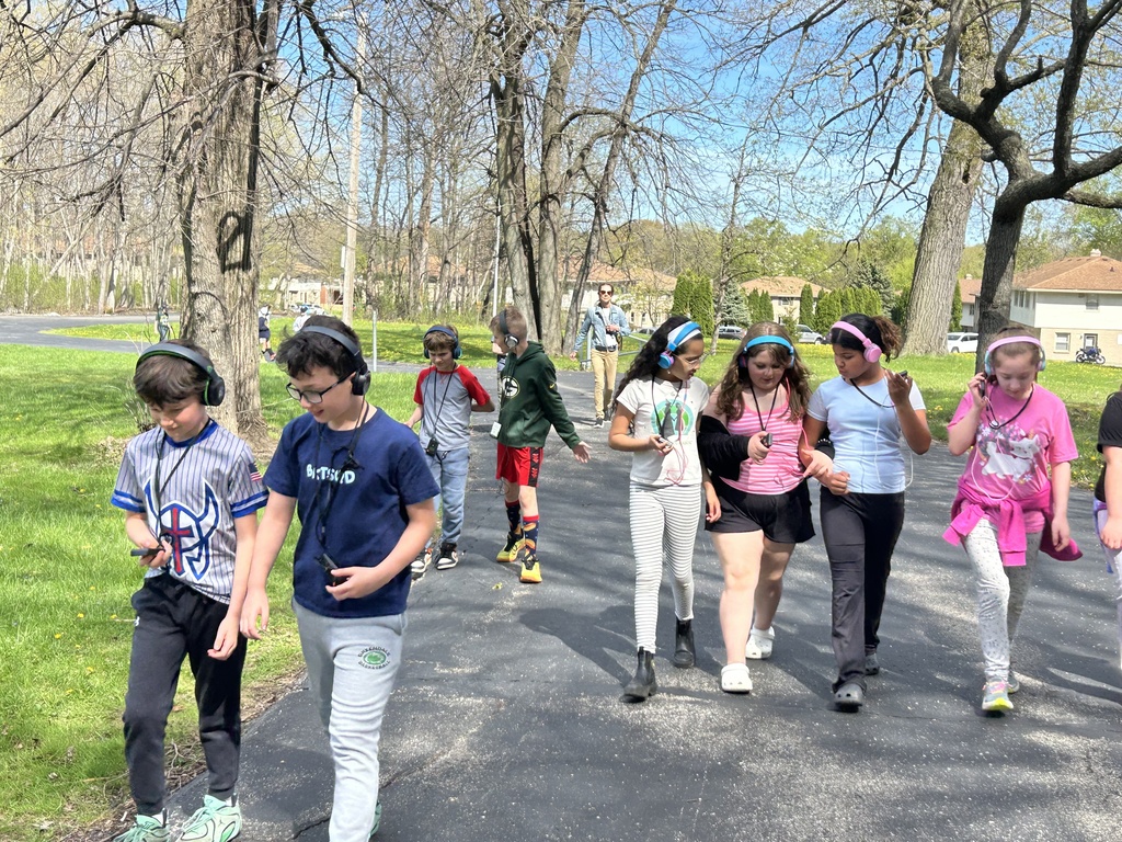 A group of students with headphones walking on a sidewalk during a Walking Classroom experience.