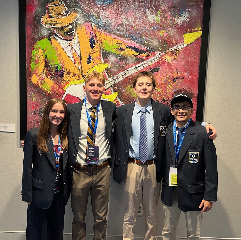 Four DECA students in their blazers posing in front of a piece if art depicting music.