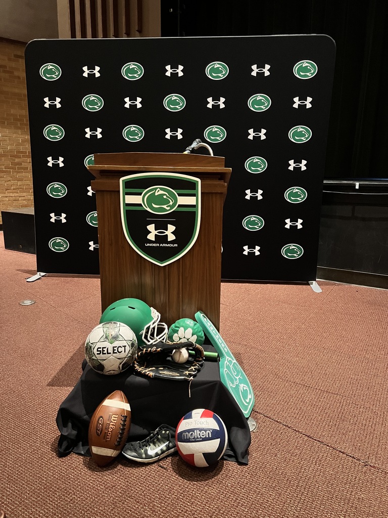 Photo of a backstop with the Greendale and Under Armor Logos and athletic balls in front of a podium.