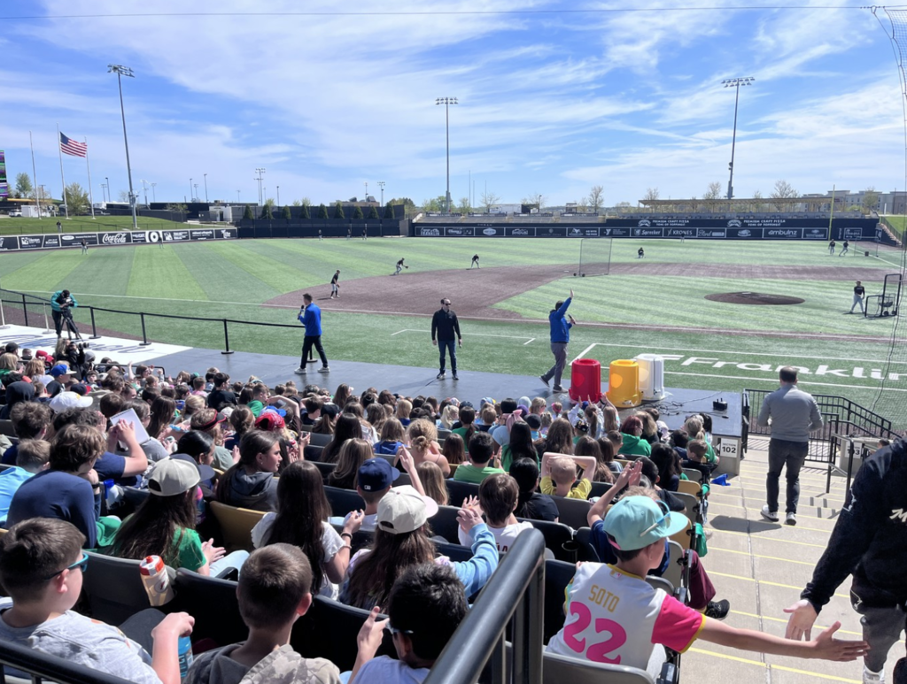 Shot of baseball field with players in action and students in the stands watching the game.
