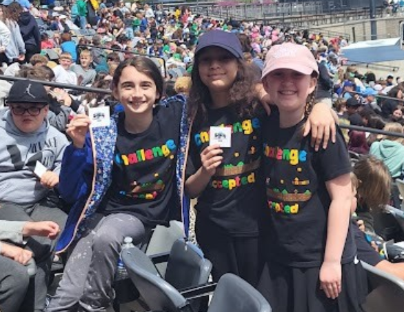 Three students posing and smiling in the stands at Franklin Field during a baseball field trip.