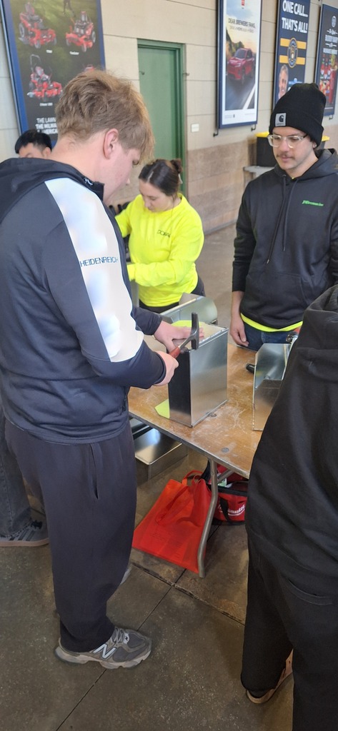 GHS student working with metal and a hammer under the supervision of a professional at a career fair.