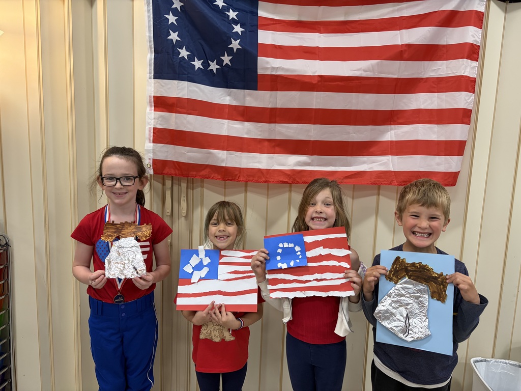 Four students smiling for the camera wearing red white and blue clothing and holding their Americana artwork