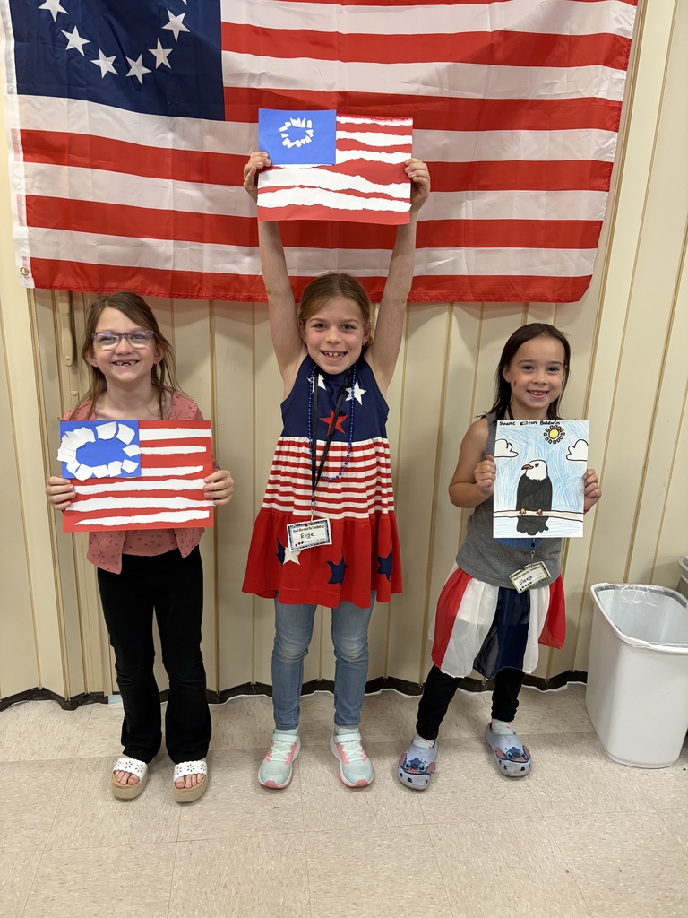 Three students holding their Americana art work standing in front of a flag