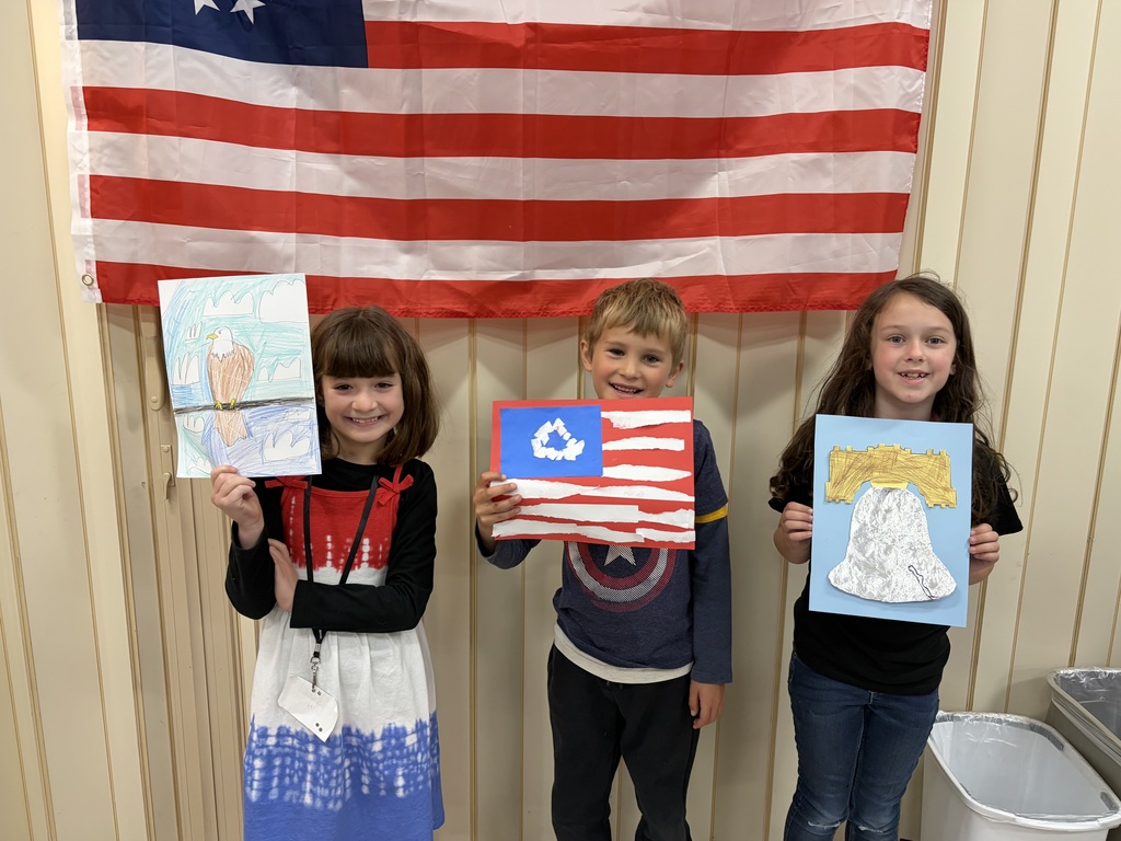 Three students holding their Americana art work standing in front of a flag