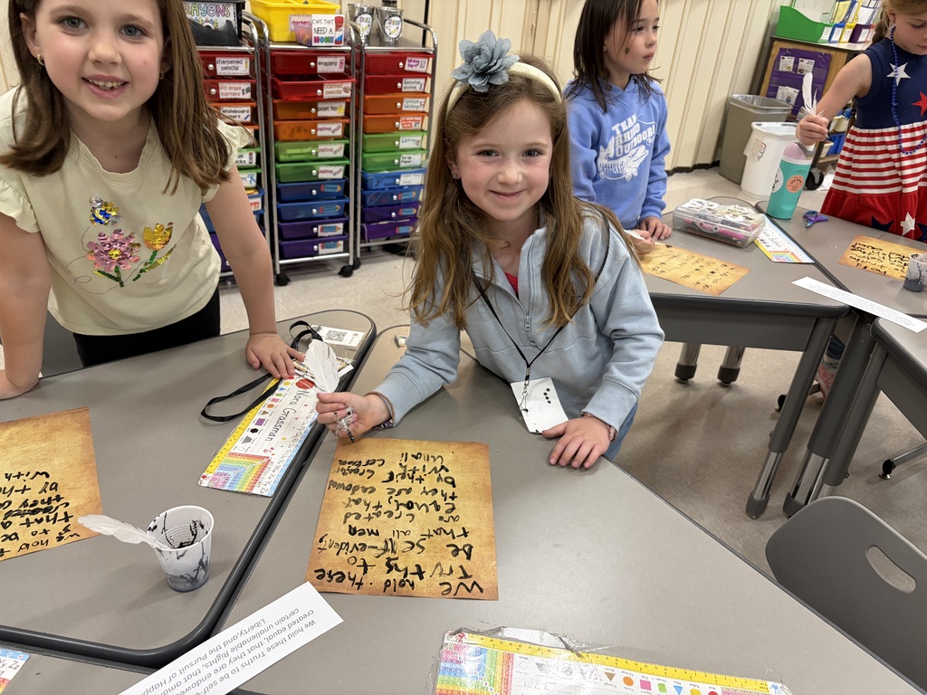 Students writing on parchment and smiling for the camera