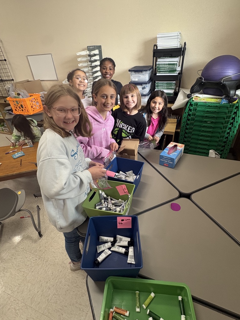 Students smiling at the camera while preparing personal hygiene kits.