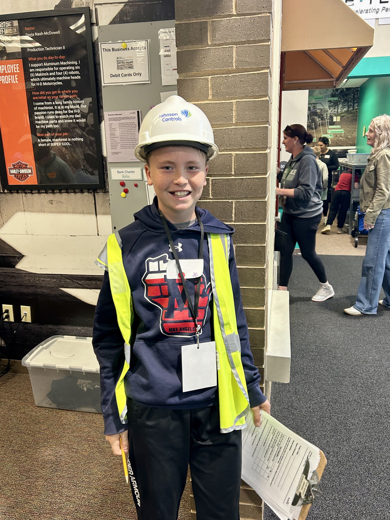 Student in a hard hat, and safety vest holding a clipboard at a work simulation at Biztown